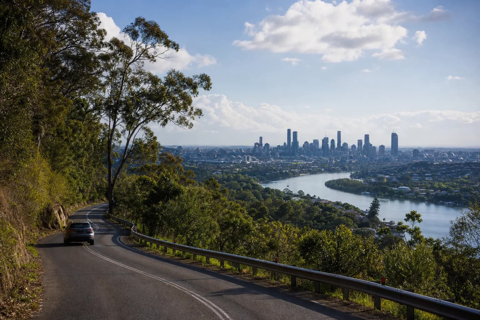 A rental car descending through subtropical greenery toward Brisbane and its river