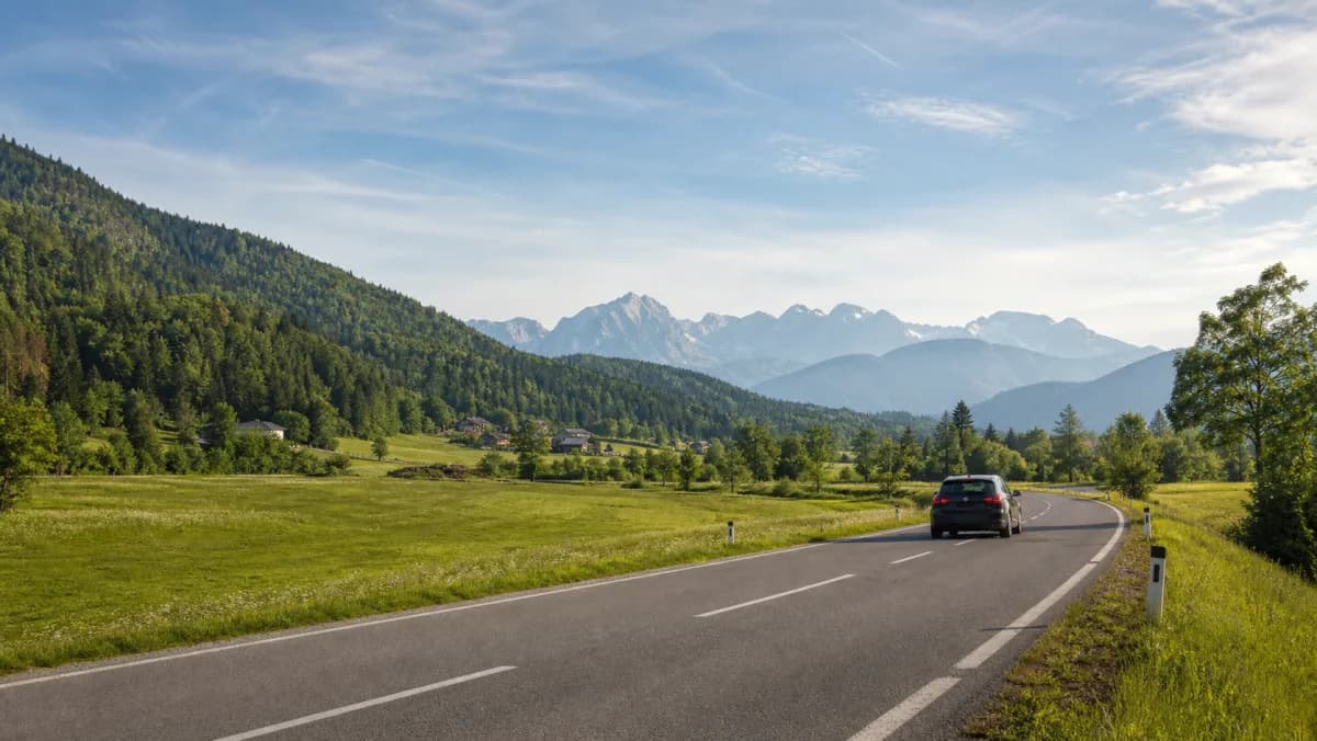 Rental car on an alpine road beside green hills in Slovenia
