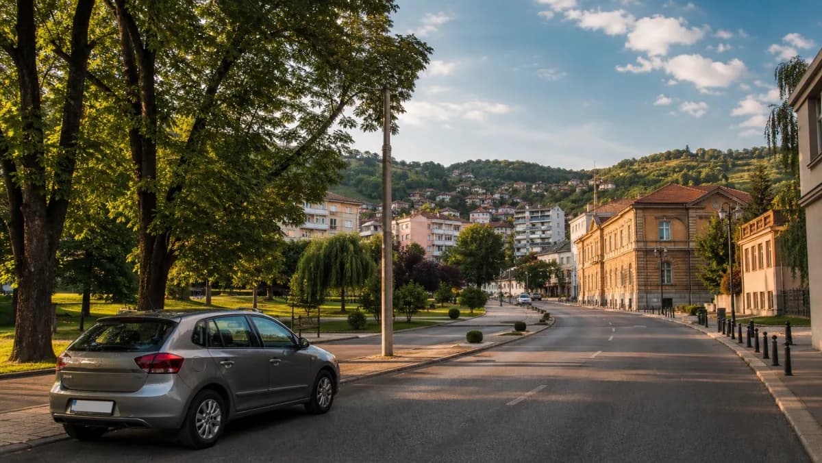 Compact rental car on a tree-lined Tuzla city road beside the city park and rolling hills