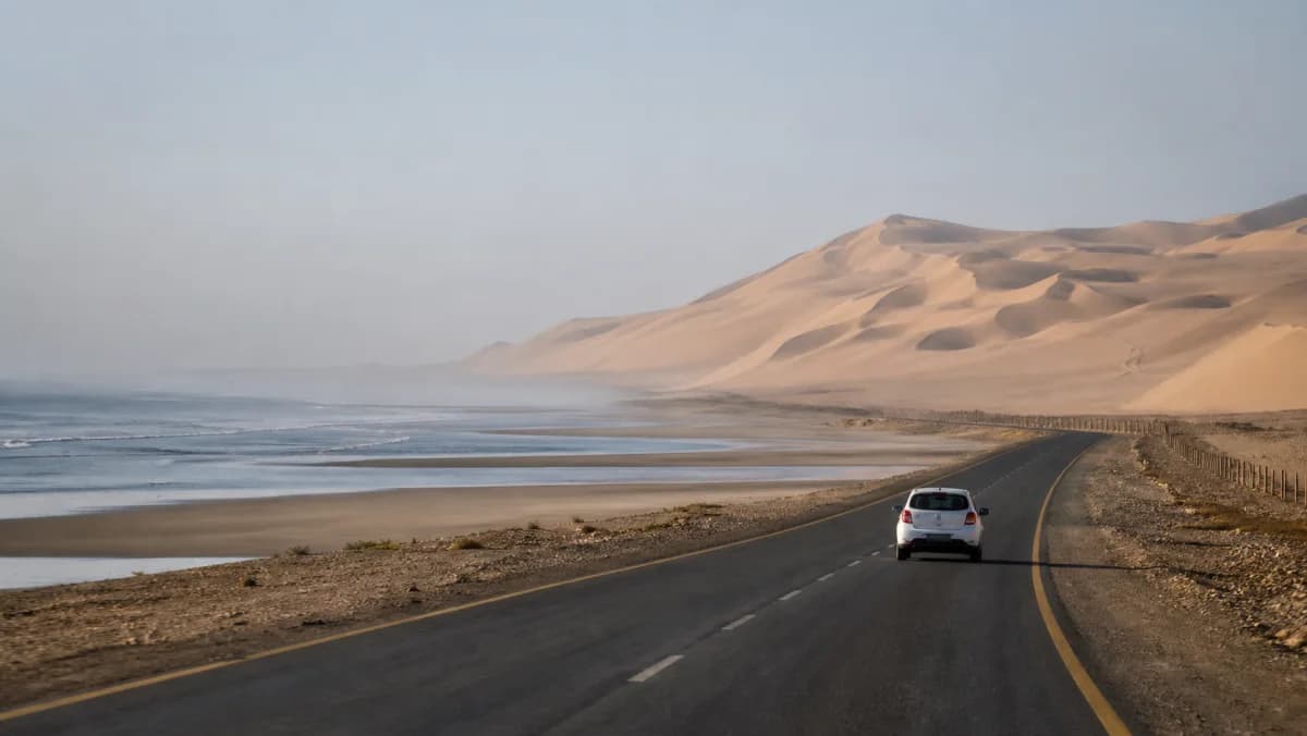 Rental car on a coastal road near Walvis Bay with Namibian dunes and Atlantic haze