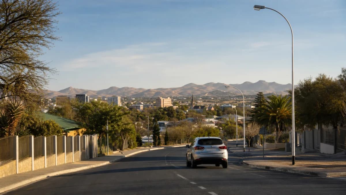 Rental car parked on a Windhoek city street with dry highland hills in the distance