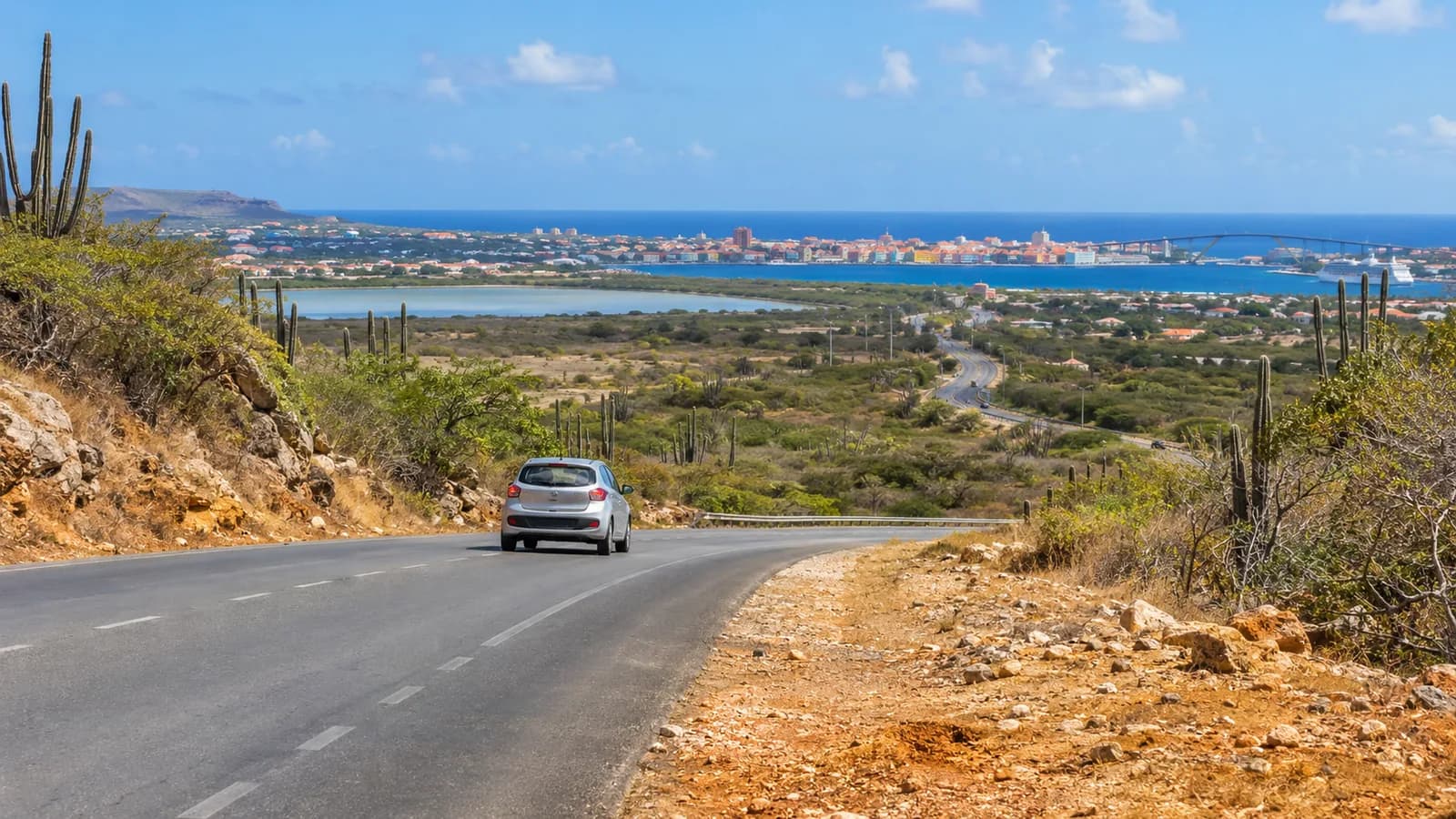 Curaçao Airport car rental illustration of an unbranded car on a dry Caribbean island road.